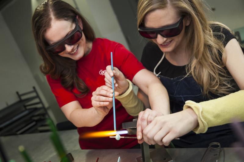 Two women work together on flameworking a glass bead